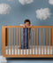 Child standing in a wooden crib wearing an ergoPouch Sleeping Bag 1.0 TOG Starbeam