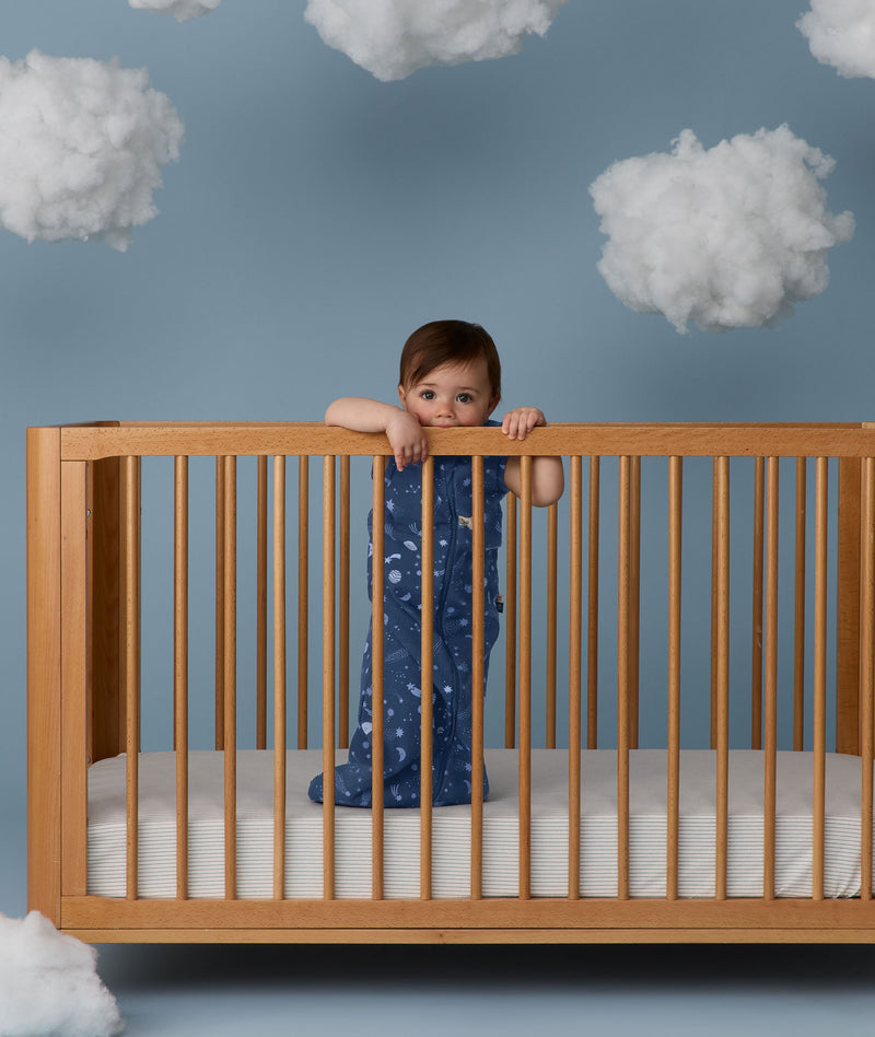 Child standing in a wooden crib wearing an ergoPouch Sleeping Bag 1.0 TOG Starbeam
