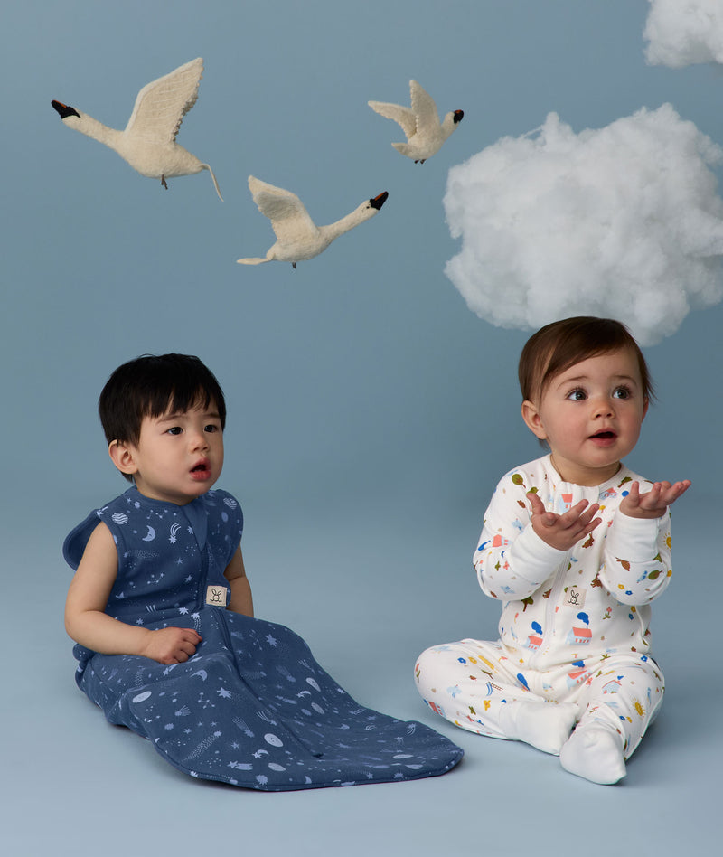 Two infants sitting in ergoPouch sleepwear, one in a Sleeping Bag 1.0 TOG Starbeam, the other in a Long Sleeve Layer 1.0 TOG Daydream.