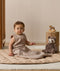 Infant wearing a sleeveless Sleeping Bag 1.0 TOG Taupe Marle, sitting on a quilted mat next to a stuffed animal.