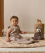 Infant wearing a sleeveless Sleeping Bag 1.0 TOG Taupe Marle, sitting on a quilted mat next to a stuffed animal.