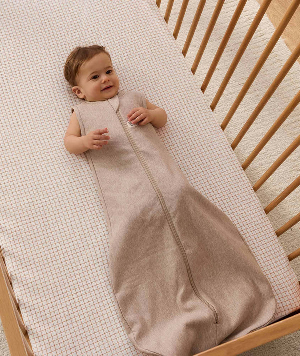 Infant lying in a wooden cot, wearing an ergoPouch Sleeping Bag  1.0 TOG Taupe Marle.