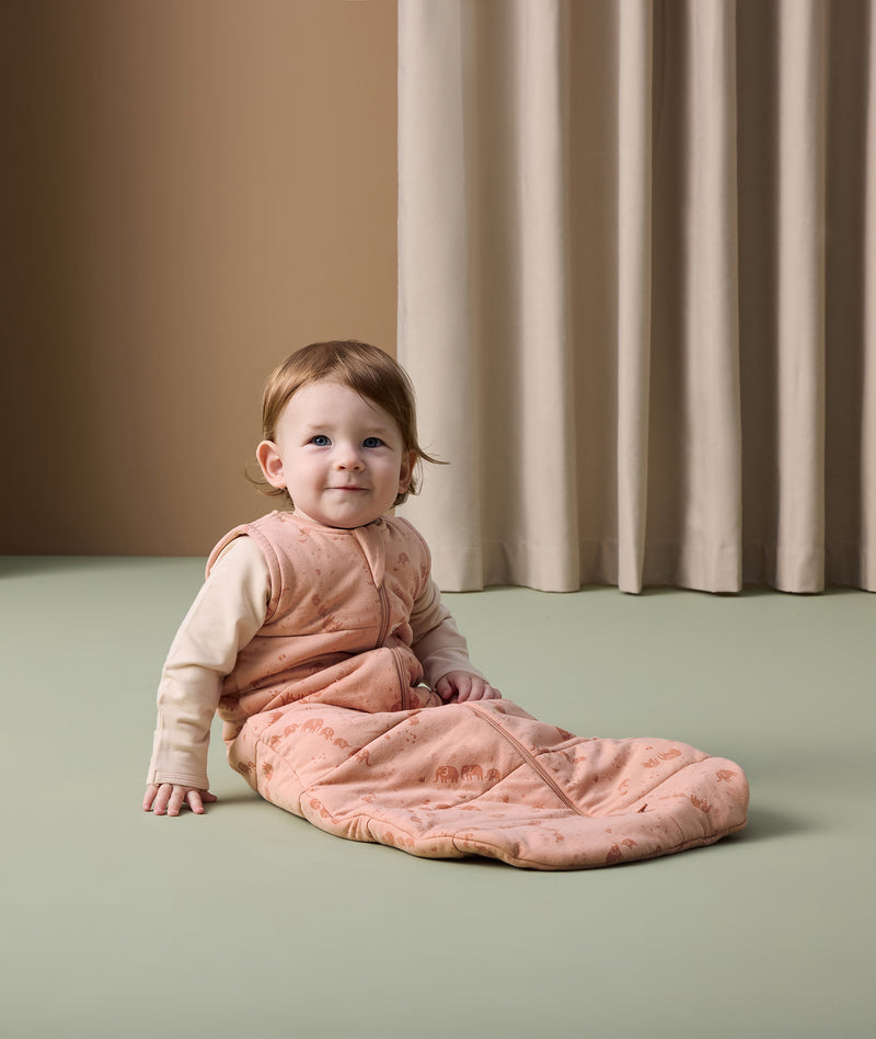 Infant sits on the floor, wearing an ergoPouch 2.5 TOG Sleeping Bag with a Long Sleeve Layer underneath.