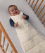 Smiling baby lying in a cot, wearing a patterned Sleeping Bag 2.5 TOG with a blue long sleeve layer underneath.