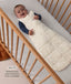 Smiling baby lying in a cot wearing a patterned ergoPouch Sleeping Bag 2.5 TOG with text highlighting slim-fit design for an easy transition from swaddling.