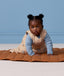 Baby wearing a printed beige sleeveless Sleeping Bag over a blue long-sleeve layer crawling on a quilted mat.