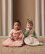 Two babies sits on a rug, each wearing ergoPouch Sleeping Bag in Elephant Parade and Savannah colourways.