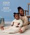 Preschooler sitting on a rug holding a baby wearing a cream patterned Sleeping Bag, with text highlighting wash-and-wear care and TOG ratings for temperature control.