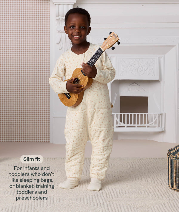 Preschooler standing and holding a ukulele, wearing a cream patterned slim-fit Sleep Onesie, with text explaining its design for toddlers and preschoolers.