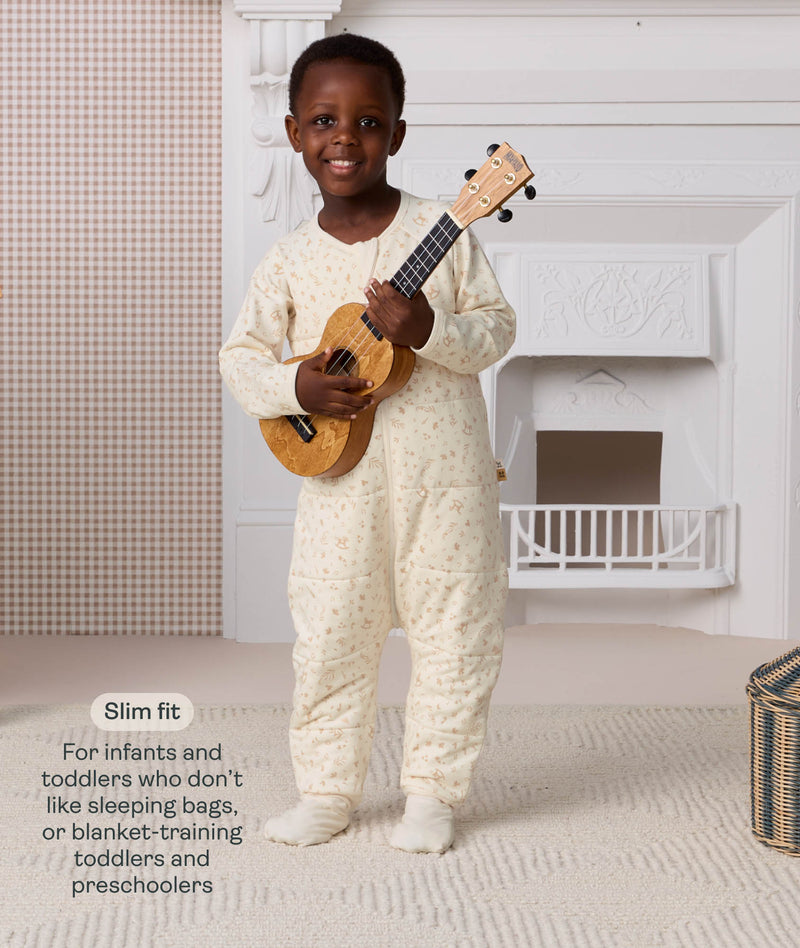 Preschooler standing and holding a ukulele, wearing a cream patterned slim-fit Sleep Onesie, with text explaining its design for toddlers and preschoolers.