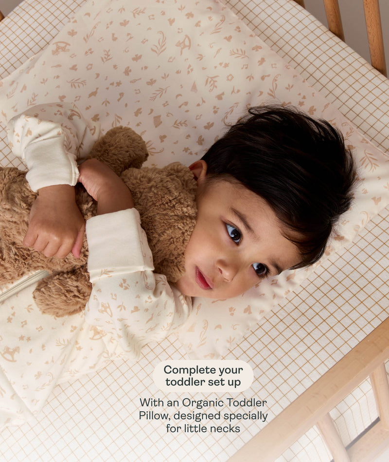 Toddler lying on a printed pillow hugging a stuffed teddy bear, with promotional text overlay reading 
