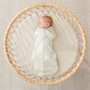 Baby sleeping in a round bassinet wearing an ergoPouch Cocoon Swaddle Bag 1.0 TOG Fawn