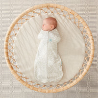Baby sleeping in a round bassinet wearing an ergoPouch Cocoon Swaddle Bag 1.0 TOG Fawn