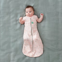 Baby wearing a Cocoon Swaddle Bag 1.0 TOG Spring Leaves, transitioning into arms out sleeping