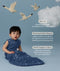 Infant wearing a ergoPouch Sleeping Bag 1.0 TOG Starbeam with text about its features on a blue background with swans and clouds.