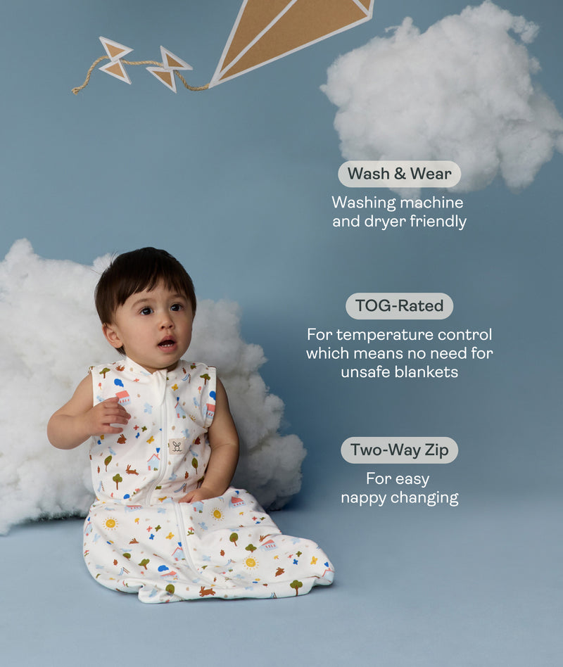 Child in an ergoPouch Sleeping Bag 1.0 TOG Daydream sitting on a blue floor with clouds and a kite, surrounded by text about product features.