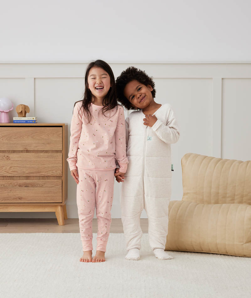 Two children in ergoPouch warm sleepwear; one in two-piece pyjamas in Daisies, and the other in Sleep Onesie 2.5 TOG Oatmeal Marle
