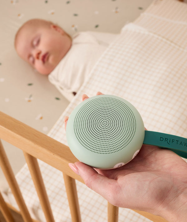 A hand holds a mint green white noise machine labeled 