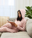 Woman wearing a light pink floral hooded Adult Sleep Onesie sitting on a sofa and writing in a notebook.