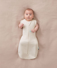 Newborn wearing an ergoPouch Cocoon Swaddle Bag 1.0 TOG Oatmeal Marle with arms out