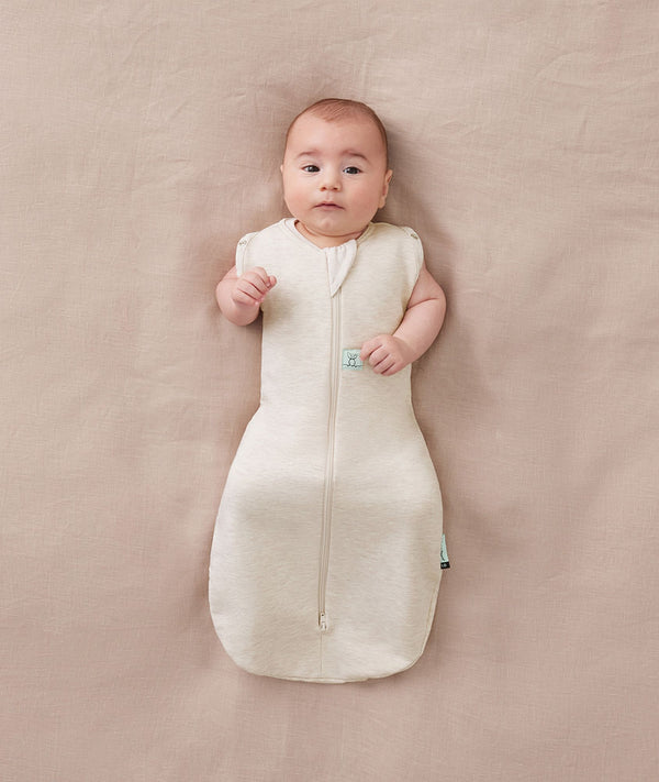 Newborn wearing an ergoPouch Cocoon Swaddle Bag 1.0 TOG Oatmeal Marle with arms out