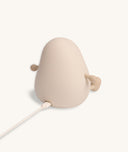 Back view of a soft-touch silicone bedtime lamp shaped like a rounded character with small arms and legs, shown plugged in with a charging cable against a plain light background.