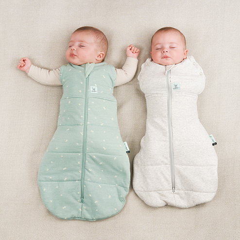 Two babies, one in a swaddle bag, the other sleeping arms out