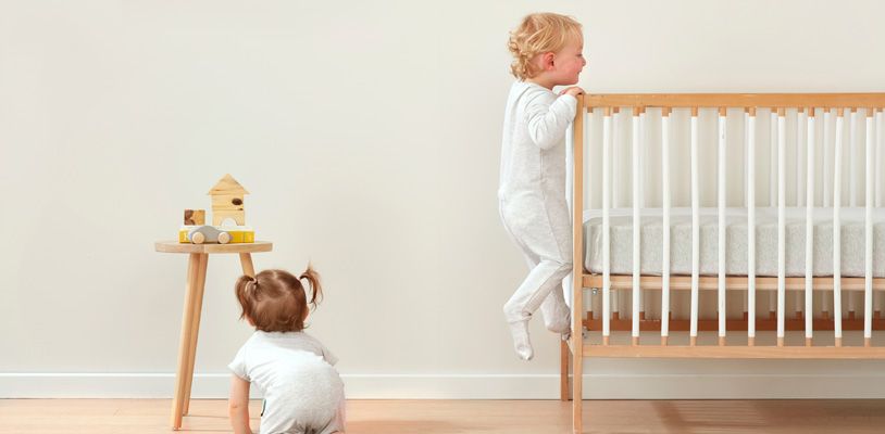 Toddler crawling out of cot while baby crawls on the floor nearby