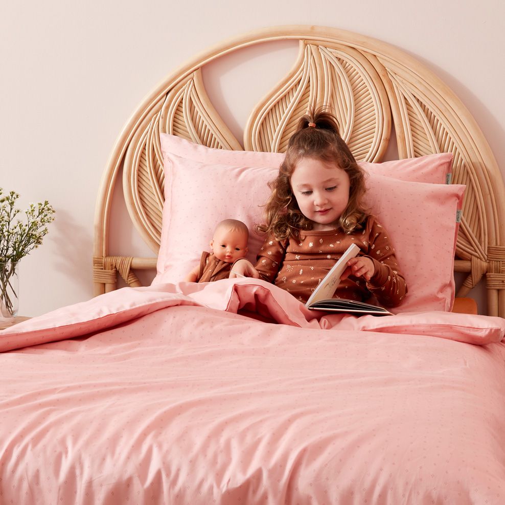 Toddler shown sitting on cot to sitting up in bed, reading a book after transitioning from cot to bed
