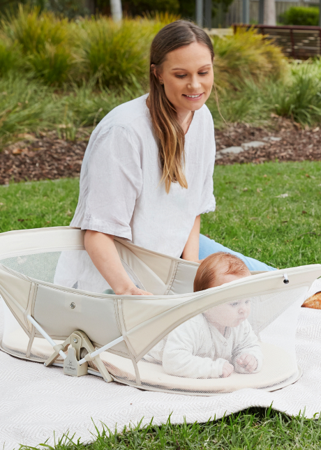 Mum sitting outside with baby in portable crib